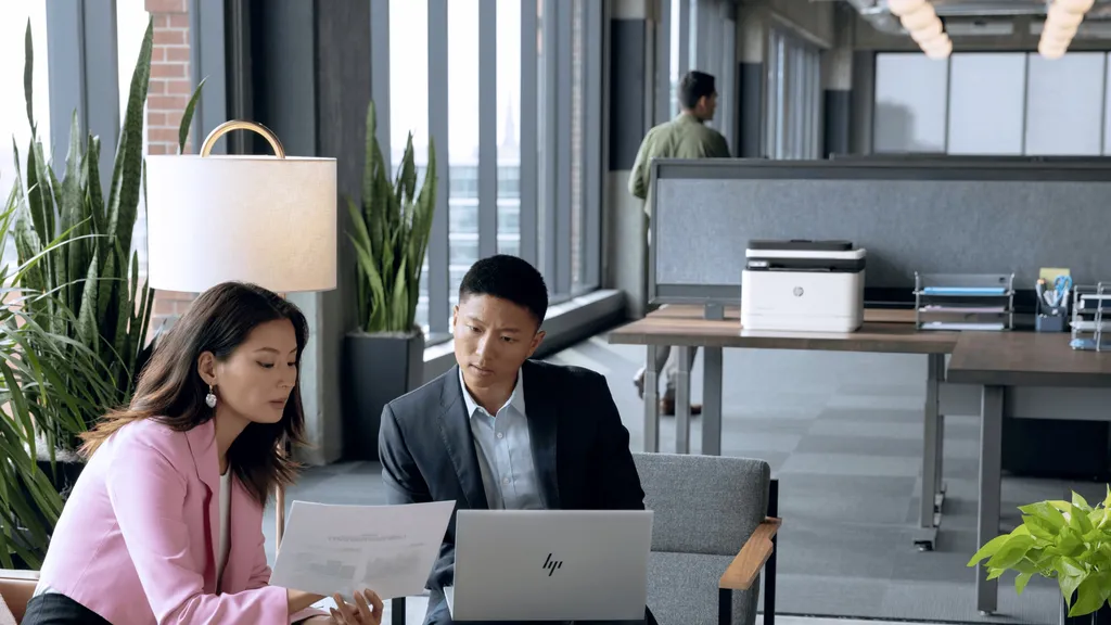 colleagues reviewing documents on an HP laptop beside a LaserJet printer in a modern office